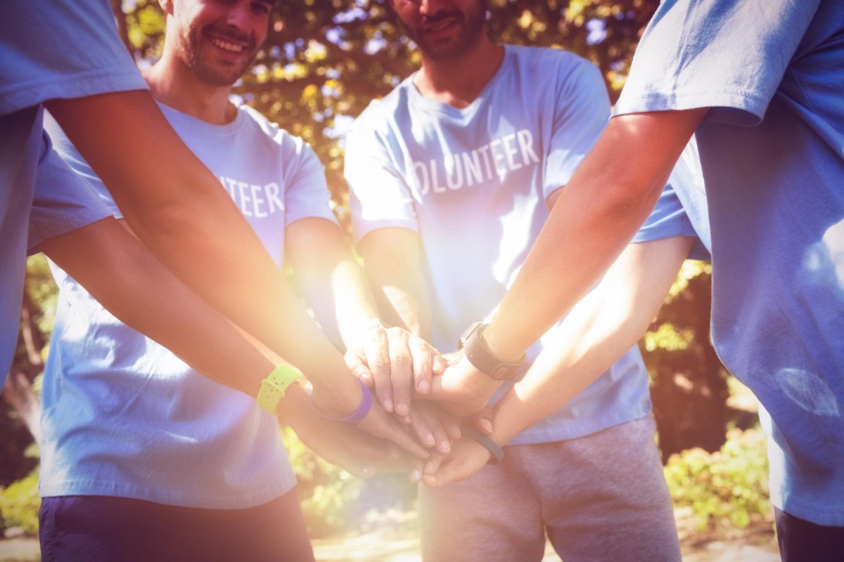 volunteers-forming-hands-stack-while-standing-park a group of people posing for the camera