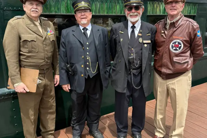 Four men in vintage military and train conductor uniforms standing on a wooden platform.