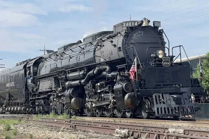 Large steam locomotive on train tracks, flying an American flag.
