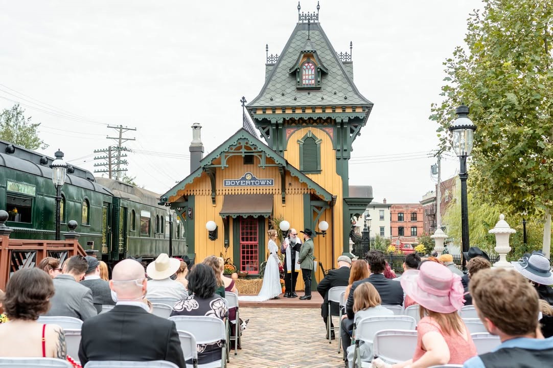 Outdoor wedding ceremony at a quaint train station with guests seated.