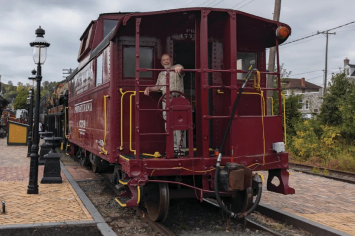 Person standing on a red train caboose at a station.